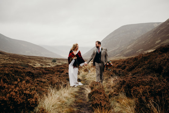 Bride and groom walk through wilderness with misty hills in background